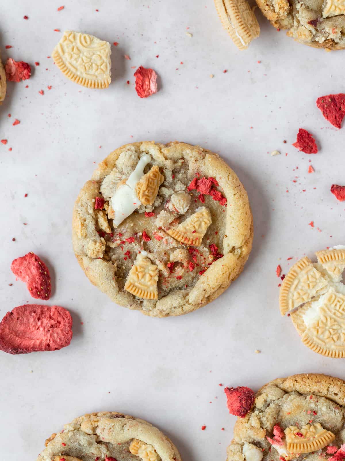 a strawberry crunch cookie surrounded by freeze dried strawberries and crushed up golden oreos on a light pink background