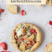 looking down on a strawberry crunch cookie on a light pink background. it says strawberry crunch cookies across the top