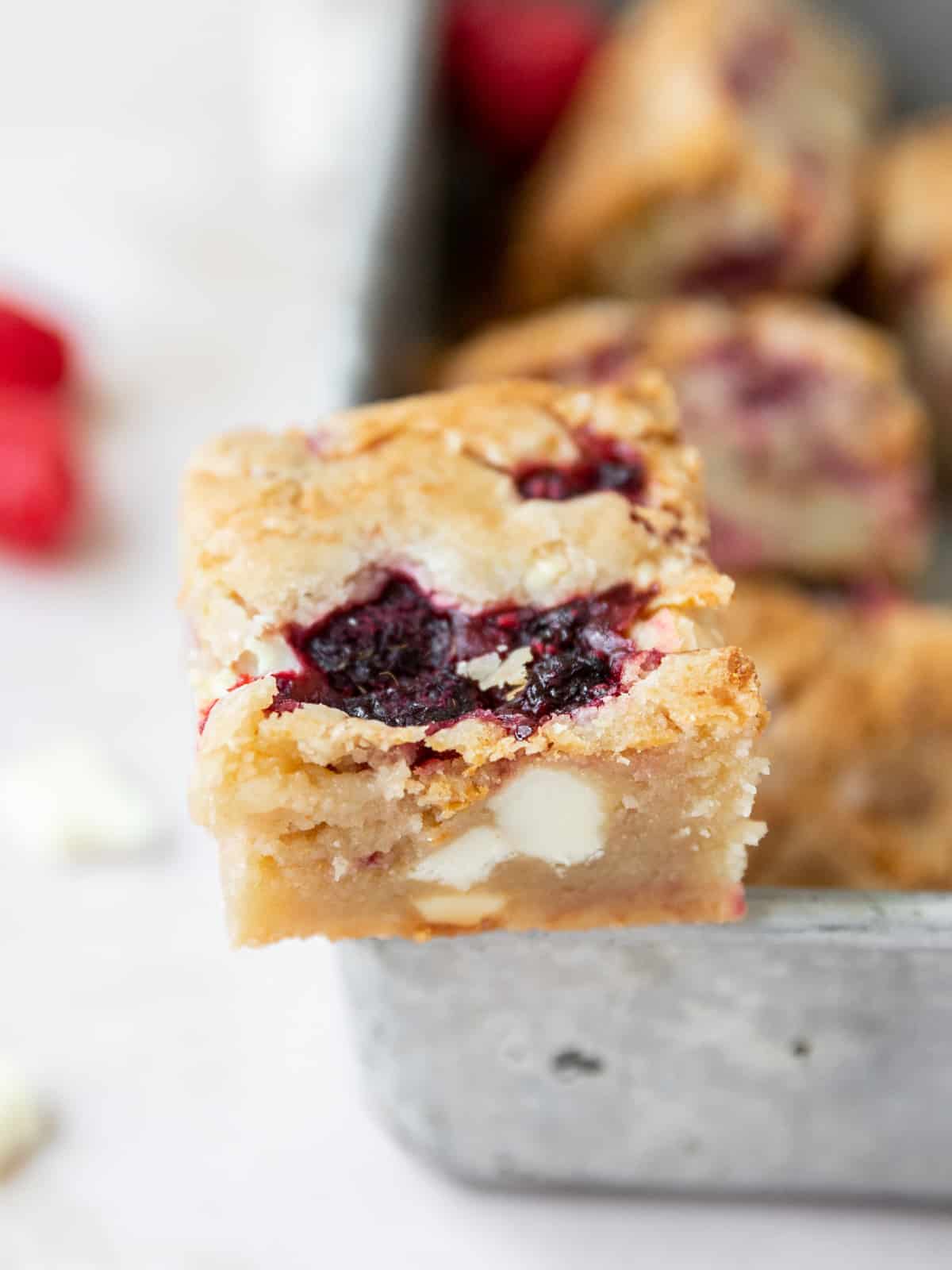 a white chocolate and raspberry blondie balanced on the edge of a metal baking dish