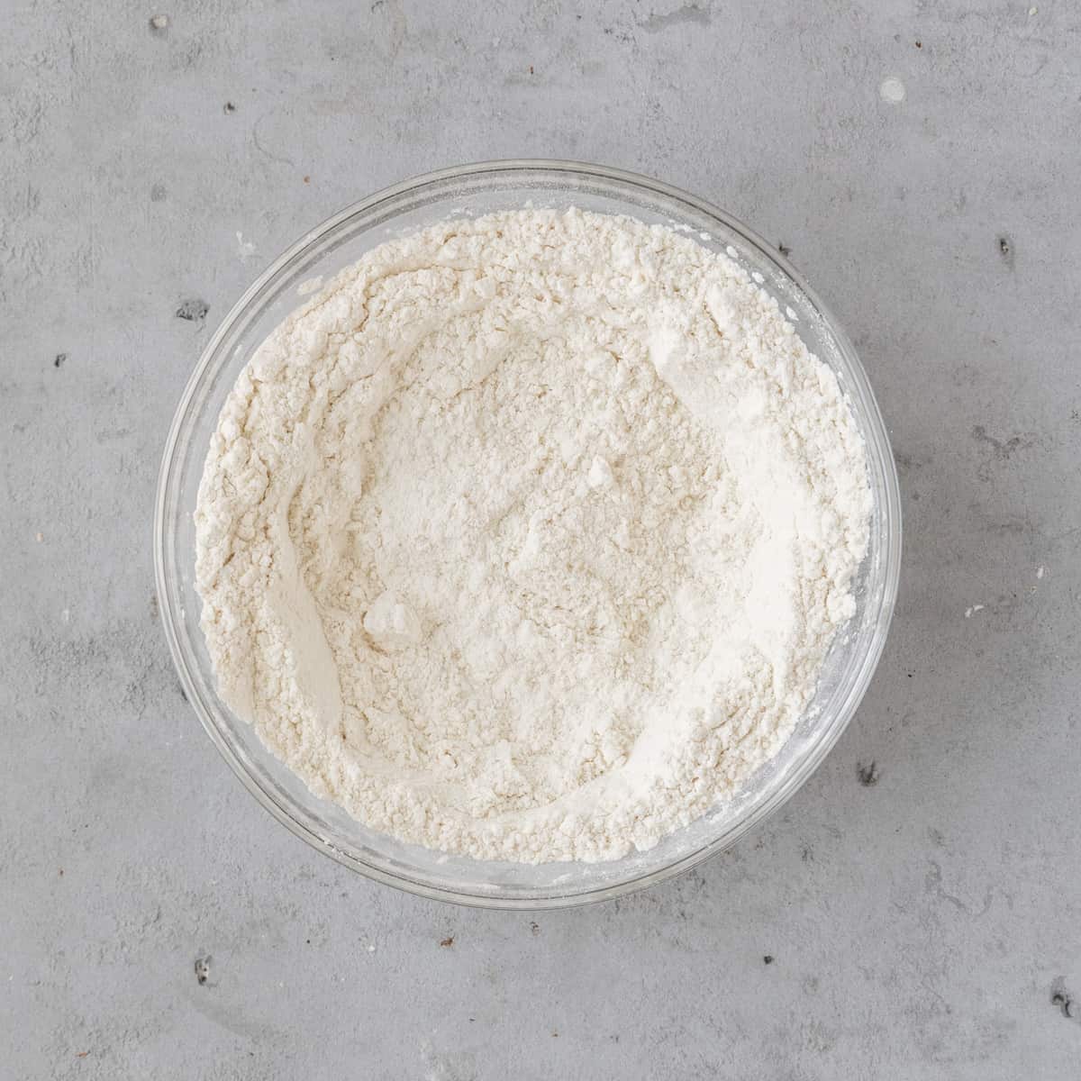 all of the dry ingredients combined in a glass bowl on a grey background