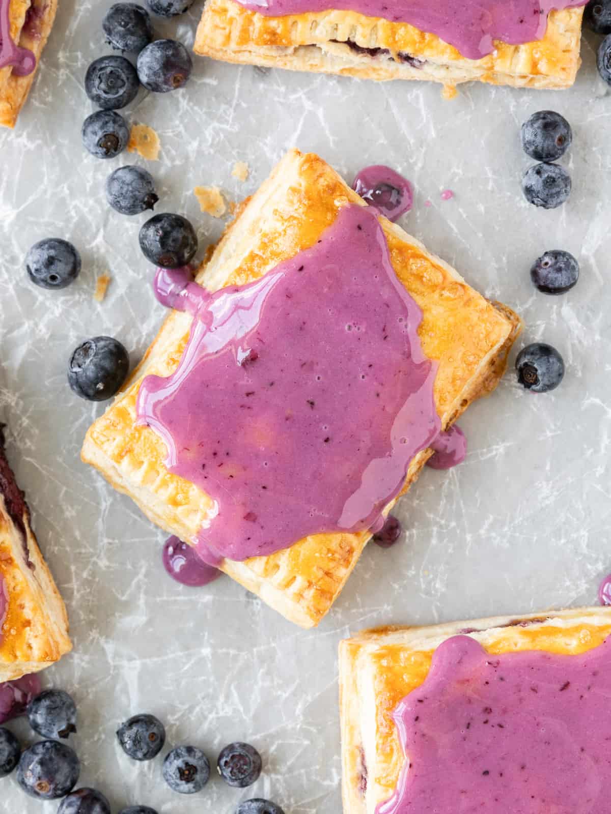 looking down on a blueberry pop tart on parchment paper surrounded by other pop tarts and fresh blueberries
