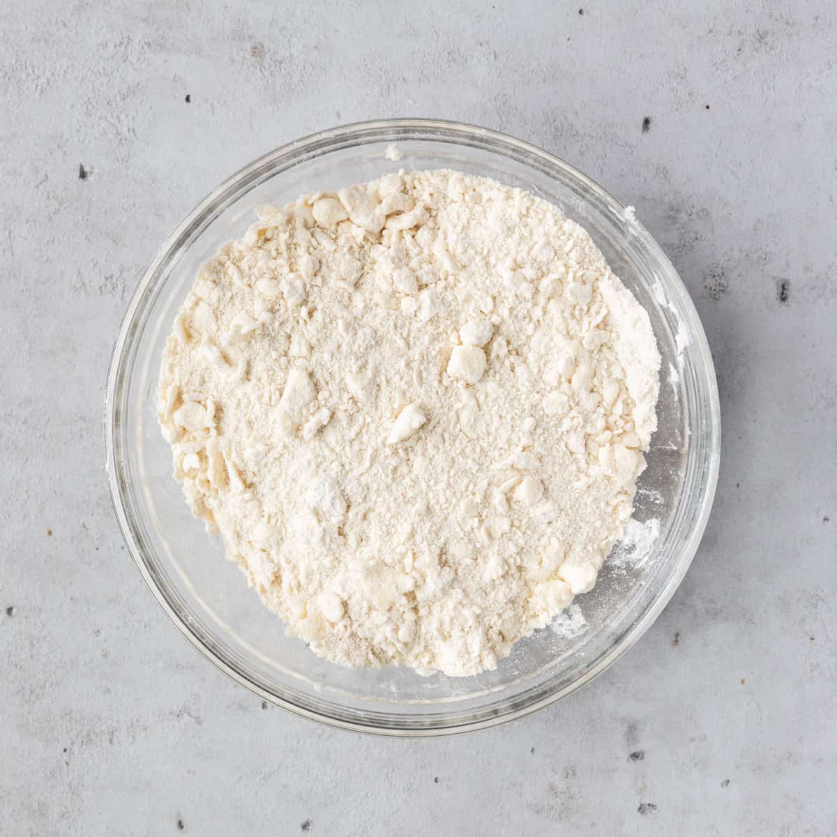 the dry ingredients and butter in a glass bowl on a grey background.