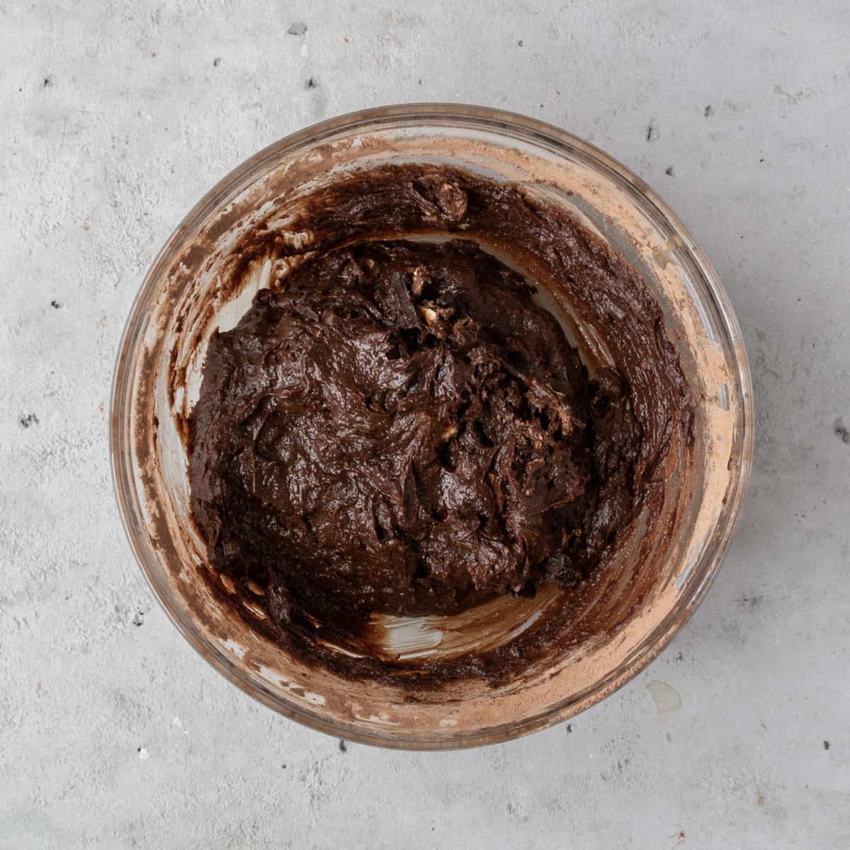the completed brownie batter in a glass bowl on a grey background.