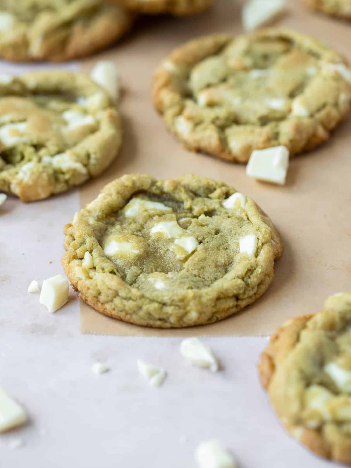 a close up of a matcha cookie surrounded by other cookies and chunks of white chocolate.