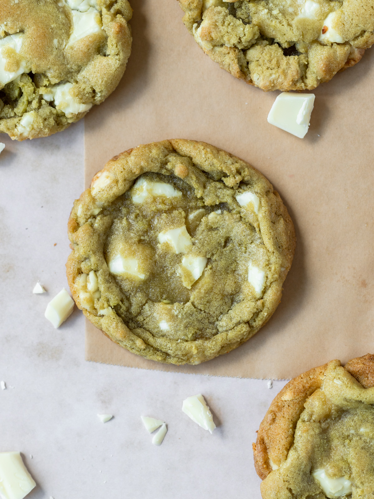 a matcha cookie on parchment paper with other cookies and white chocolate chunks around it.
