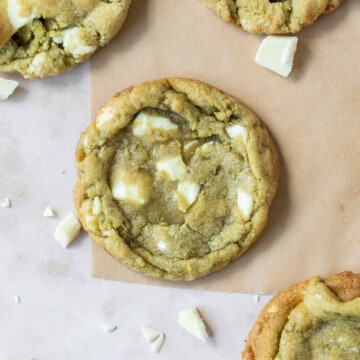 looking down on a matcha cookie on parchment paper with other cookies and white chocolate chunks around it.