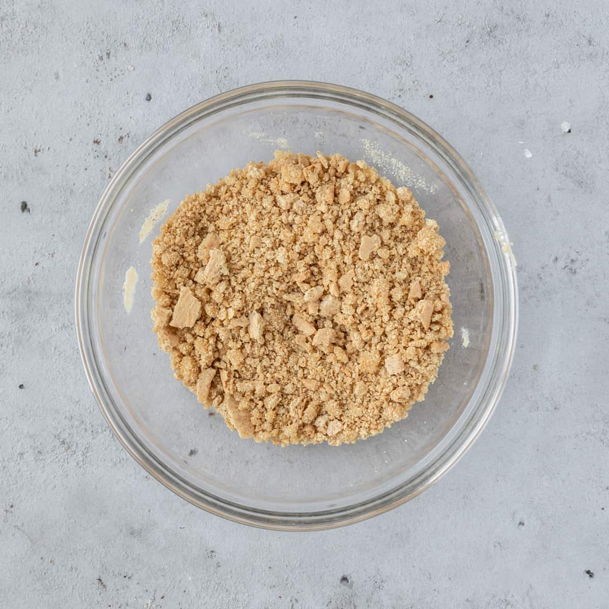 the graham cracker crust in a glass bowl on a grey background.