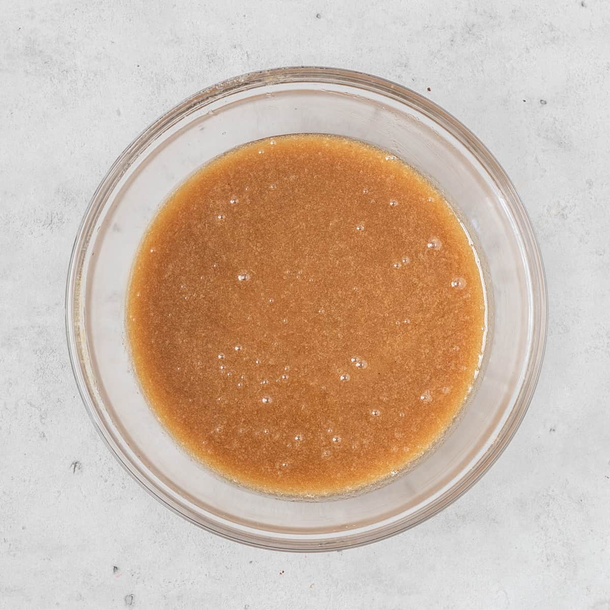 the wet ingredients and sugars combined in a glass bowl on a grey background.