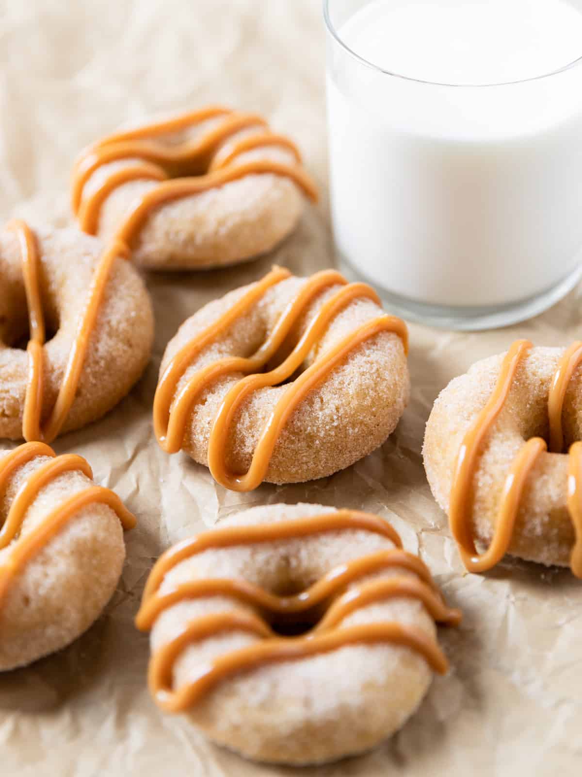 several churro donuts drizzled with dulce de leche on parchment paper with a glass of milk beside them.