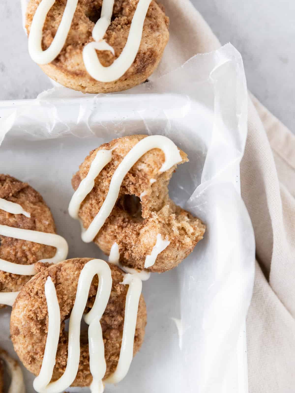 several cinnamon roll donuts in a white pan, one donut has a bite out of it.