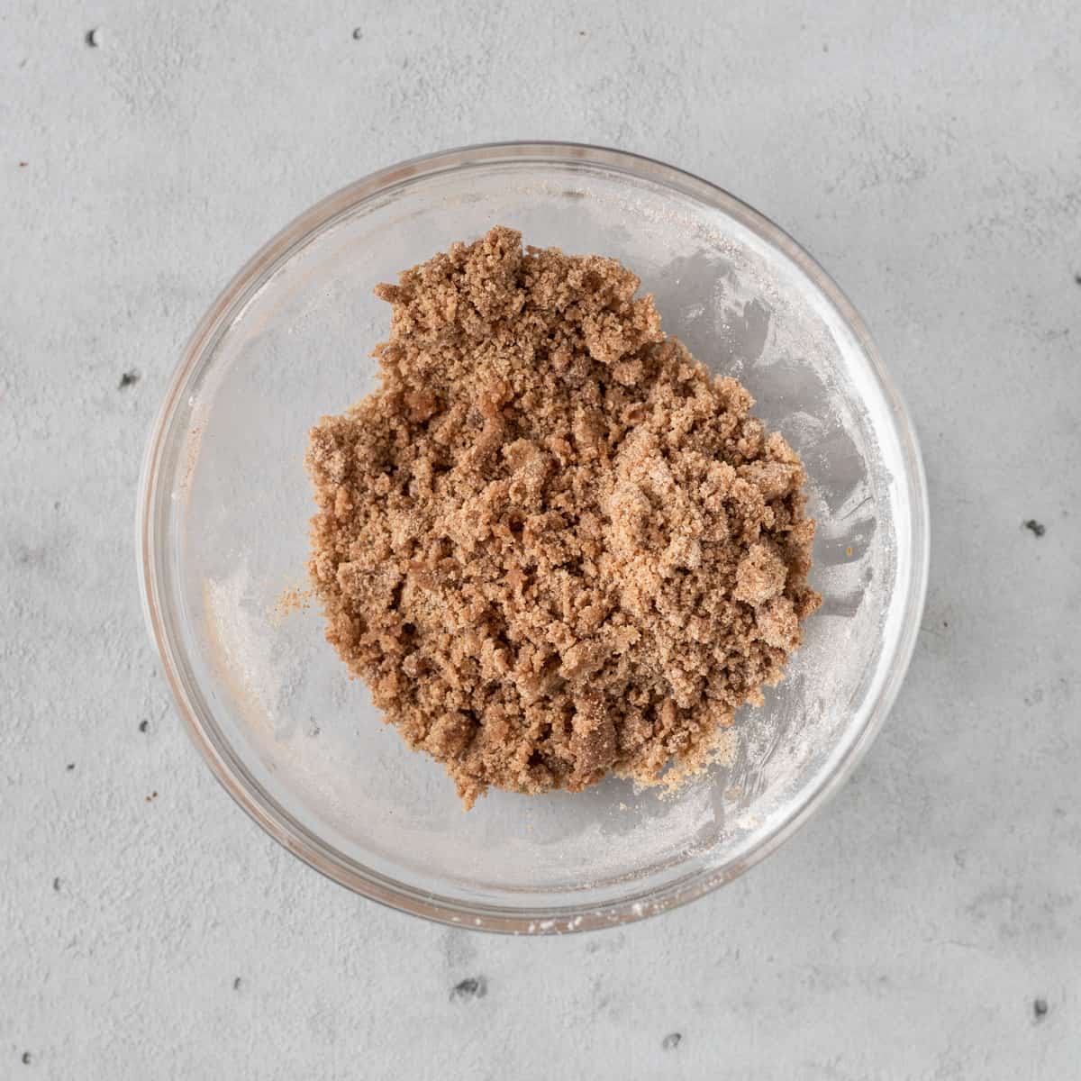 the cinnamon crumble mixture in a glass bowl on a grey background.