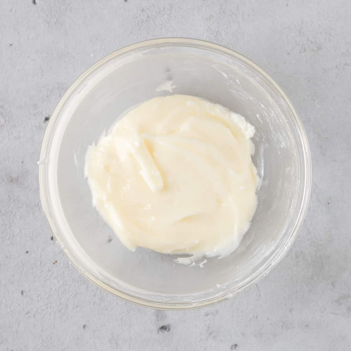 the cream cheese icing in a glass bowl on a grey background.