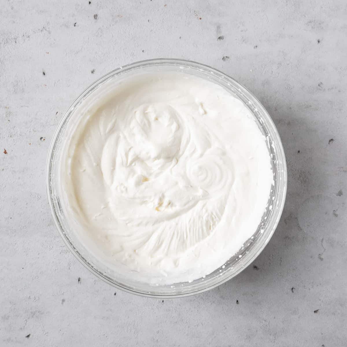 the whipped cream beat to stiff peaks in a glass bowl on a grey background.
