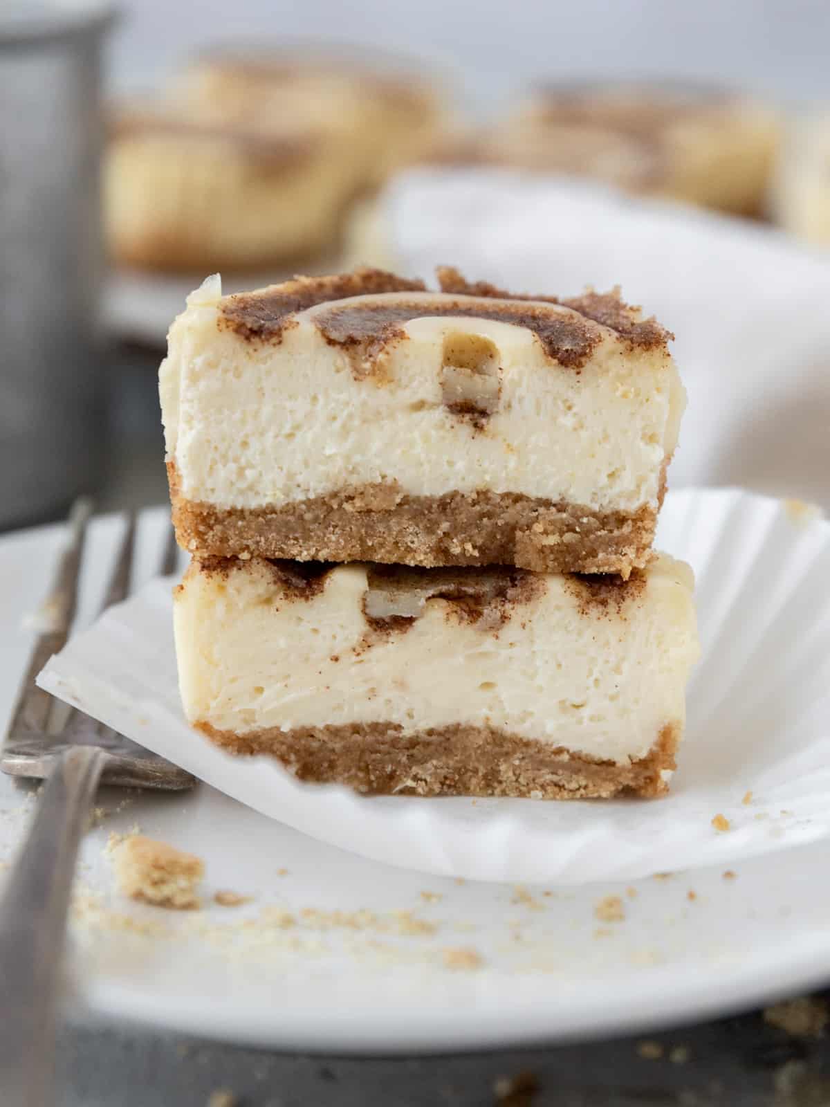 a mini cinnamon roll cheesecake cut in half and stacked on top of each other on a a grey plate with a fork next to it.