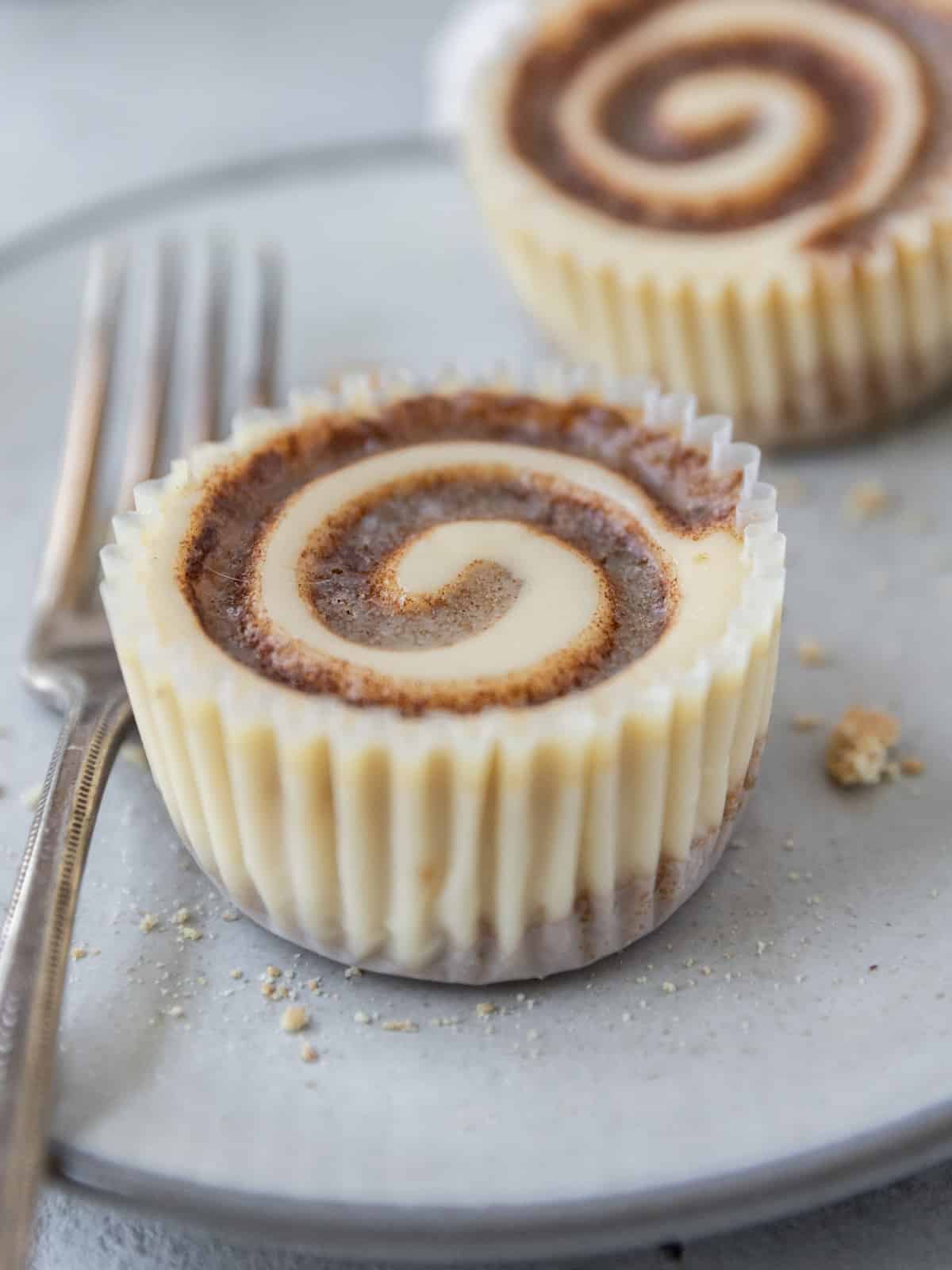 two mini cinnamon roll cheesecakes on a grey plate with a fork next to them.