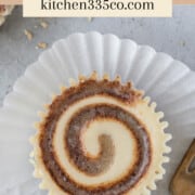 looking down on a mini cinnamon roll cheesecake laying on a cupcake liner with a fork next to it. It says mini cinnamon roll cheesecakes across the top.