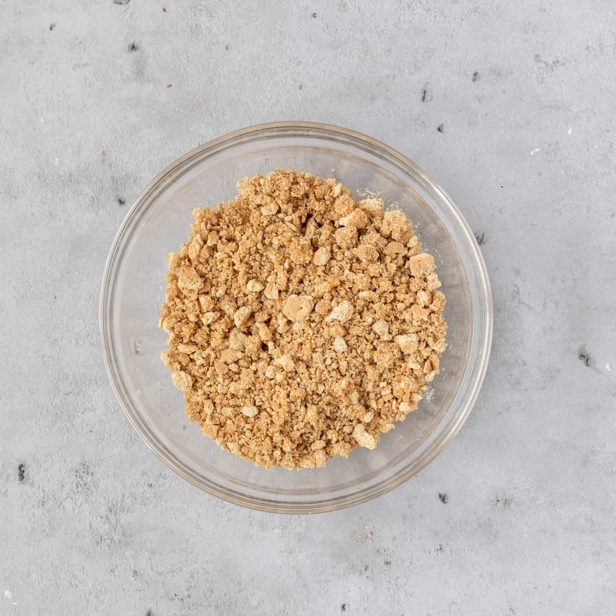 the graham cracker crust mixture in a glass bowl on a grey background.