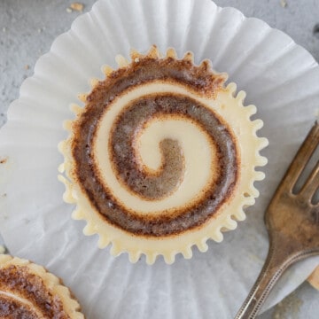 looking down on a mini cinnamon roll cheesecake laying on a cupcake liner with a fork next to it.