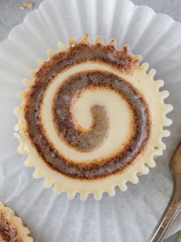looking down on a mini cinnamon roll cheesecake laying on a cupcake liner with a fork next to it.