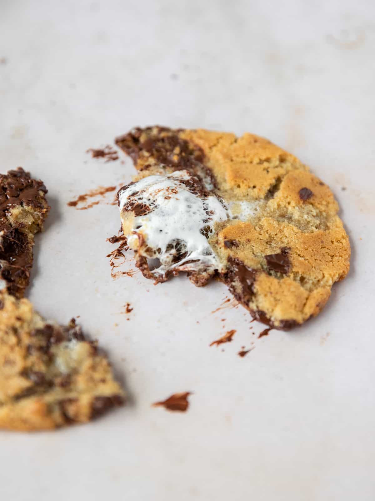 a s'mores stuffed cookie split in half with smears of chocolate by it on a tan background.