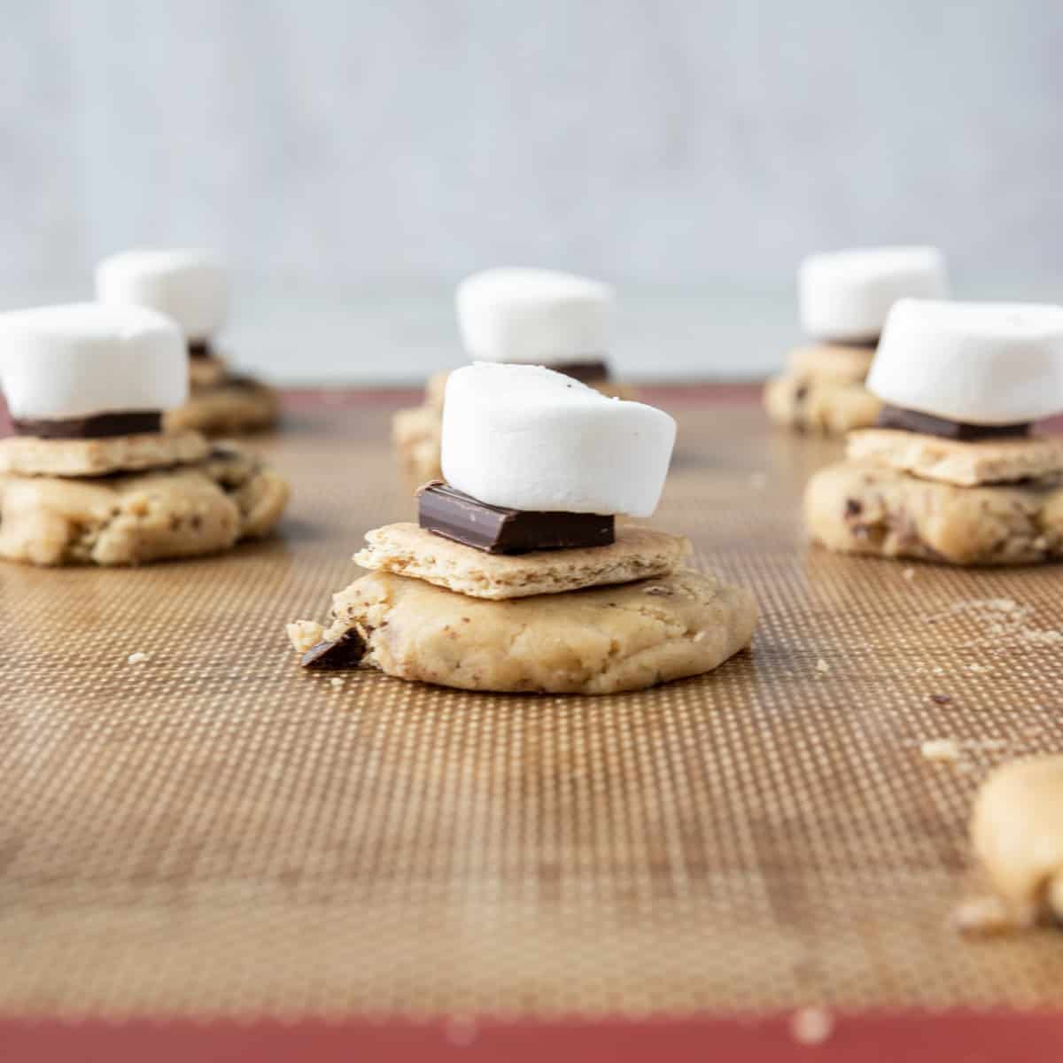 the cookie dough, graham cracker, chocolate, and marshmallow stacked on a baking sheet before being rolled up and baked.