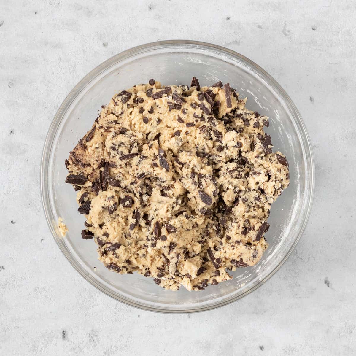 the completed chocolate chip cookie dough in a glass bowl on a grey background.