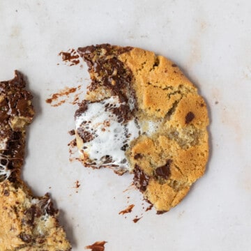 looking down on a s'mores stuffed cookie that is split in half on a tan background.