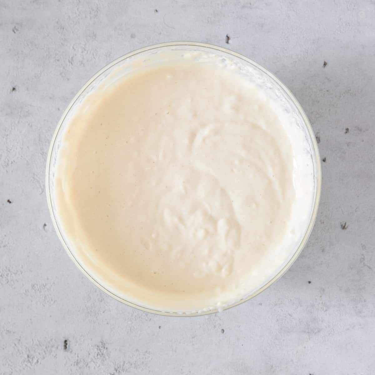 the completed pancake batter in a glass bowl on a grey background.