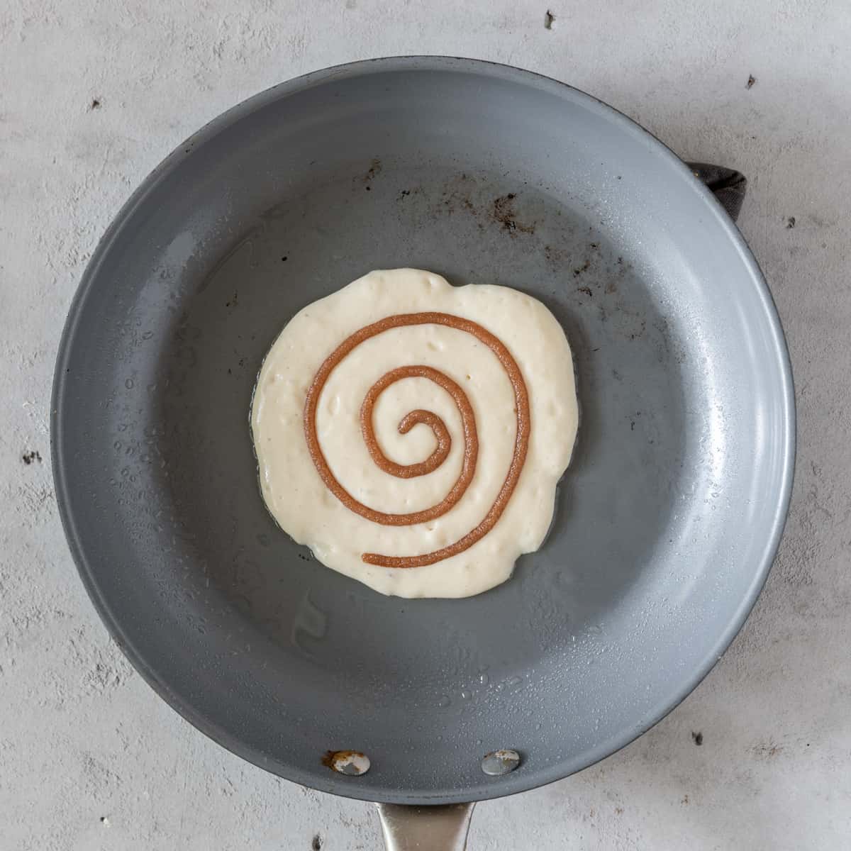 a cinnamon roll pancake being cooked on a skillet.