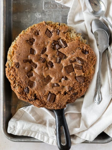 a deep dish cookie on a metal tray with a linen napkin and four spoons beside it.