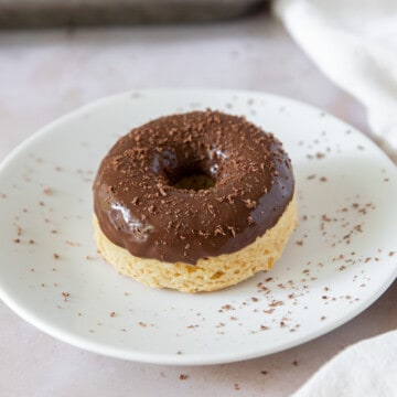 a chocolate glazed donut on a white plate that has been sprinkled with chocolate shavings.