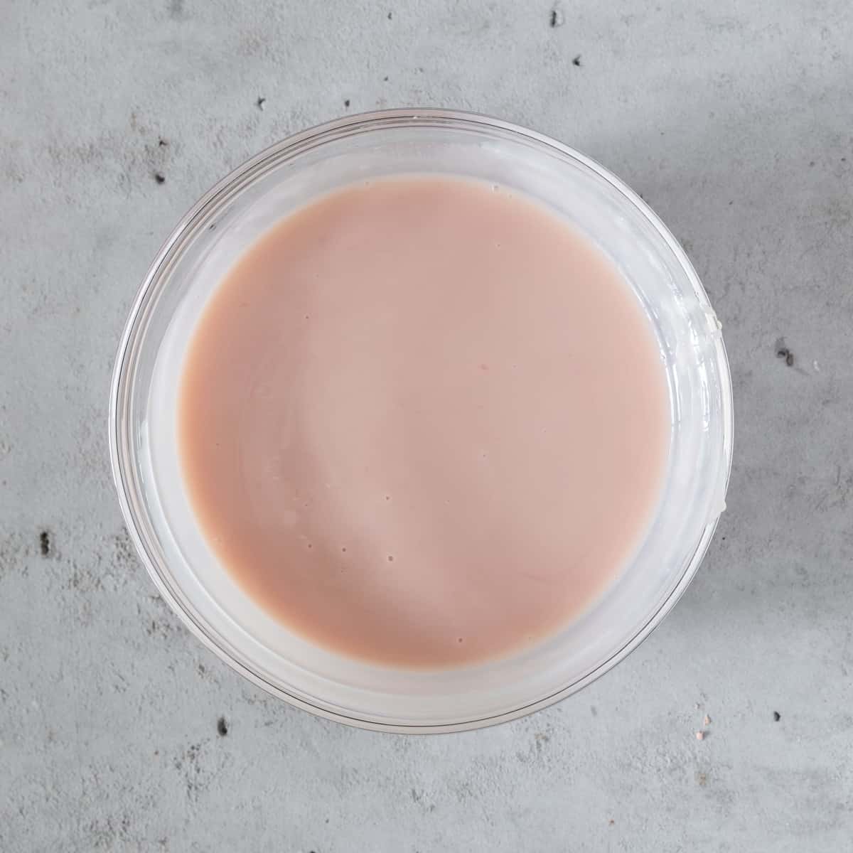 the pink lemonade concentrate and sweetened condensed milk combined in a glass bowl on a grey background.