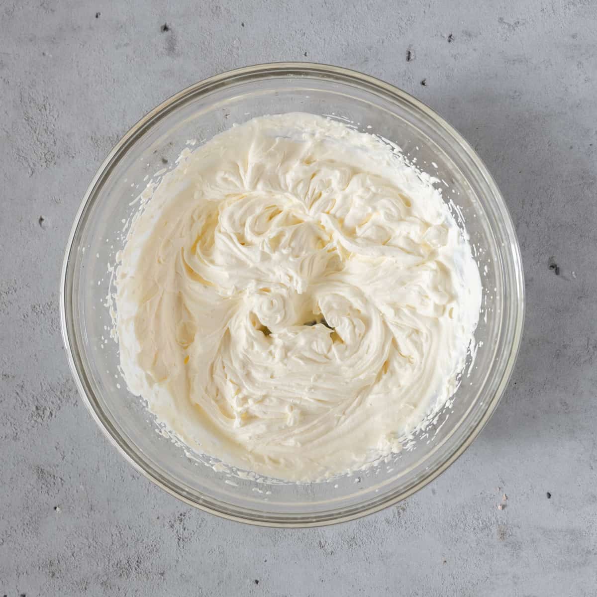 the whipped cream in a glass bowl on a grey background.