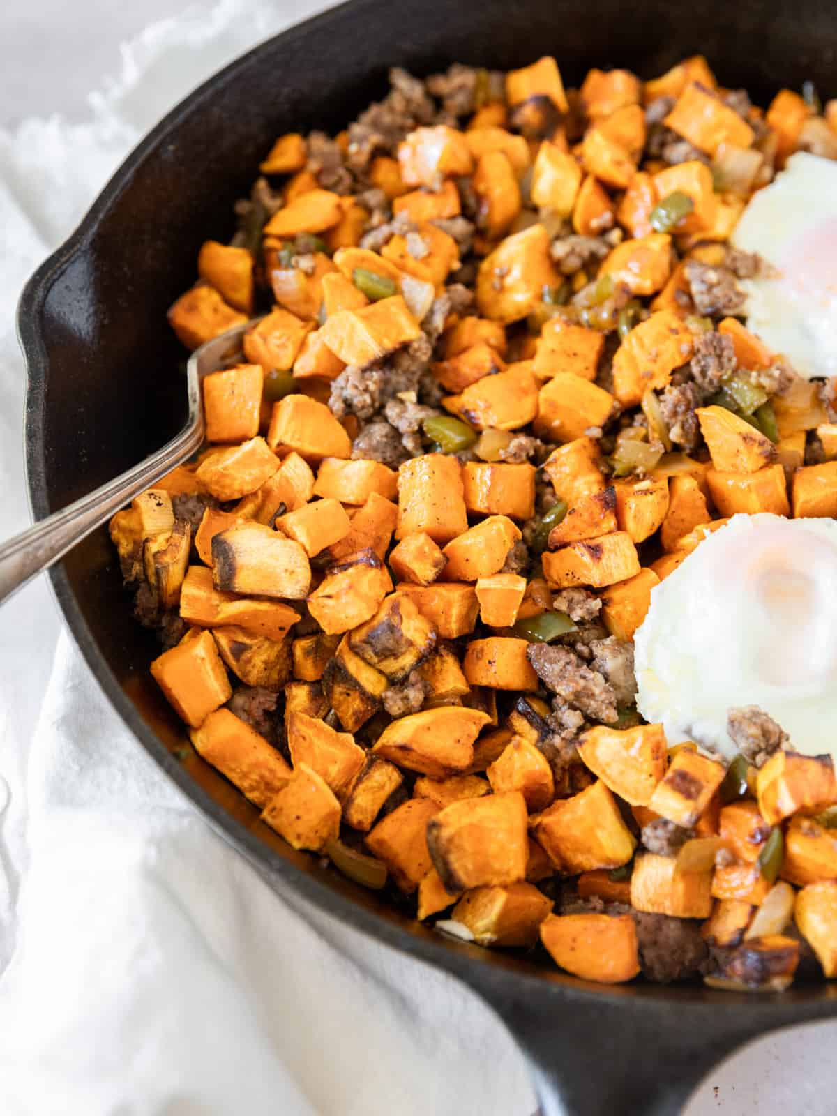 the sweet potato breakfast hash in a cast iron pan with two eggs on the side and a fork stuck into it.