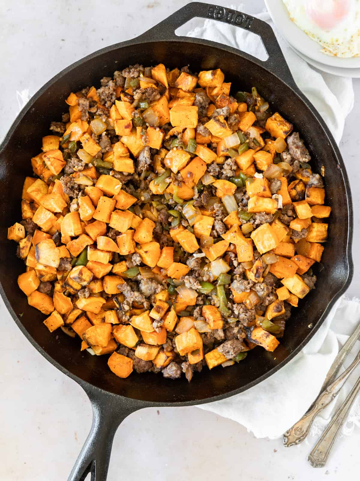 sweet potato breakfast hash in a cast iron skillet with a white linen napkin under it and three forks on the side.