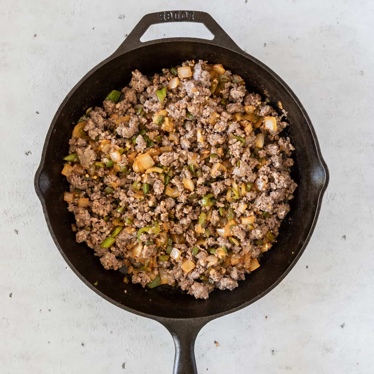 the vegetables and sausage combined in a cast iron skillet on a grey background.