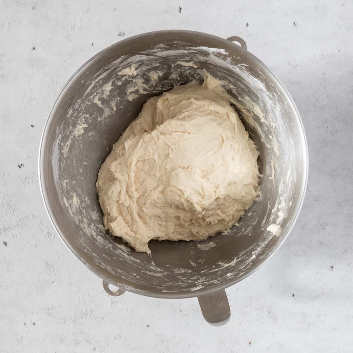 the completed dough in a metal mixing bowl on a grey background.