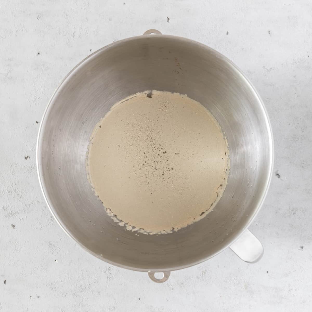 the water and instant yeast combined in a metal mixing bowl on a grey background.