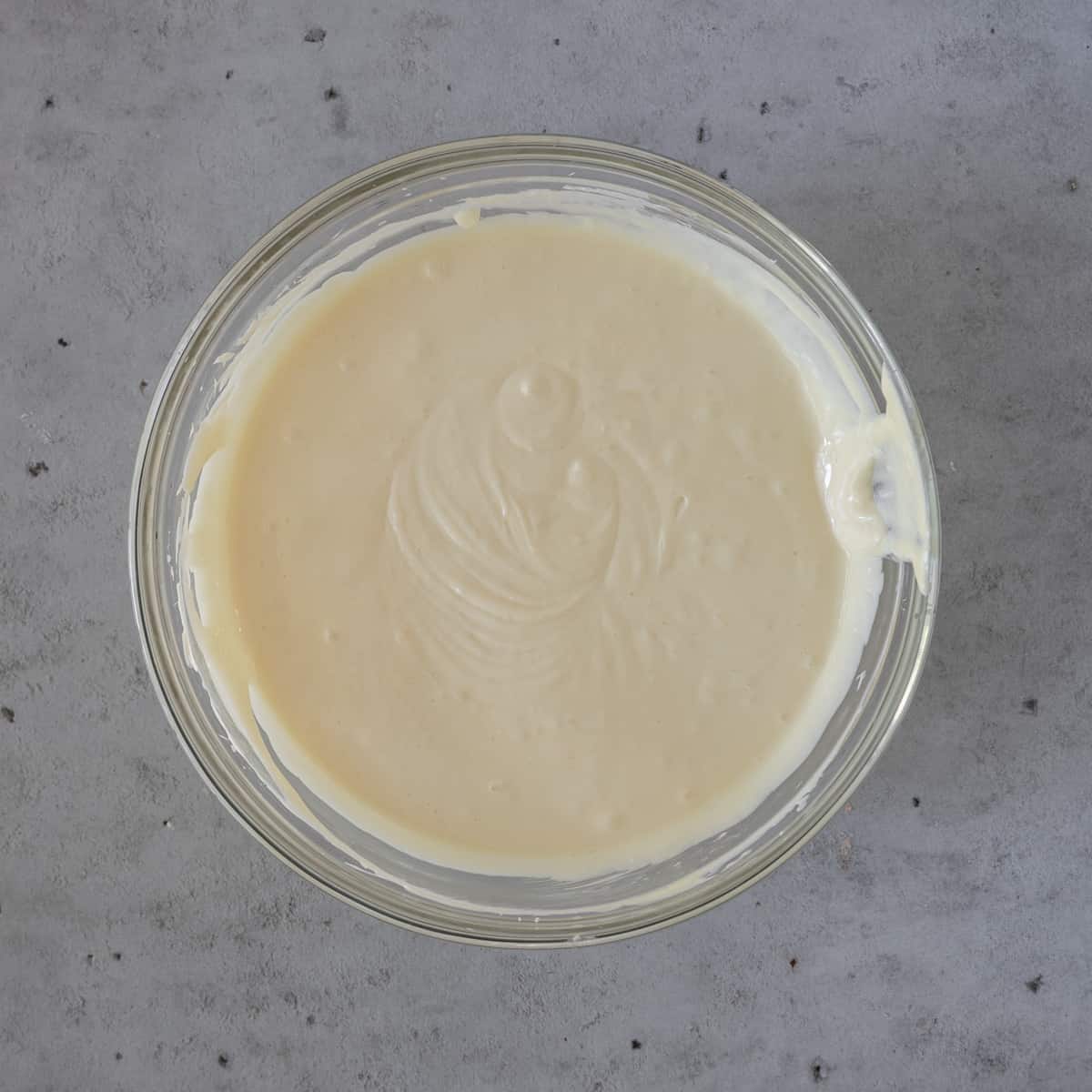 the cream cheese, sugar, and eggs combined in a glass bowl on a grey background.