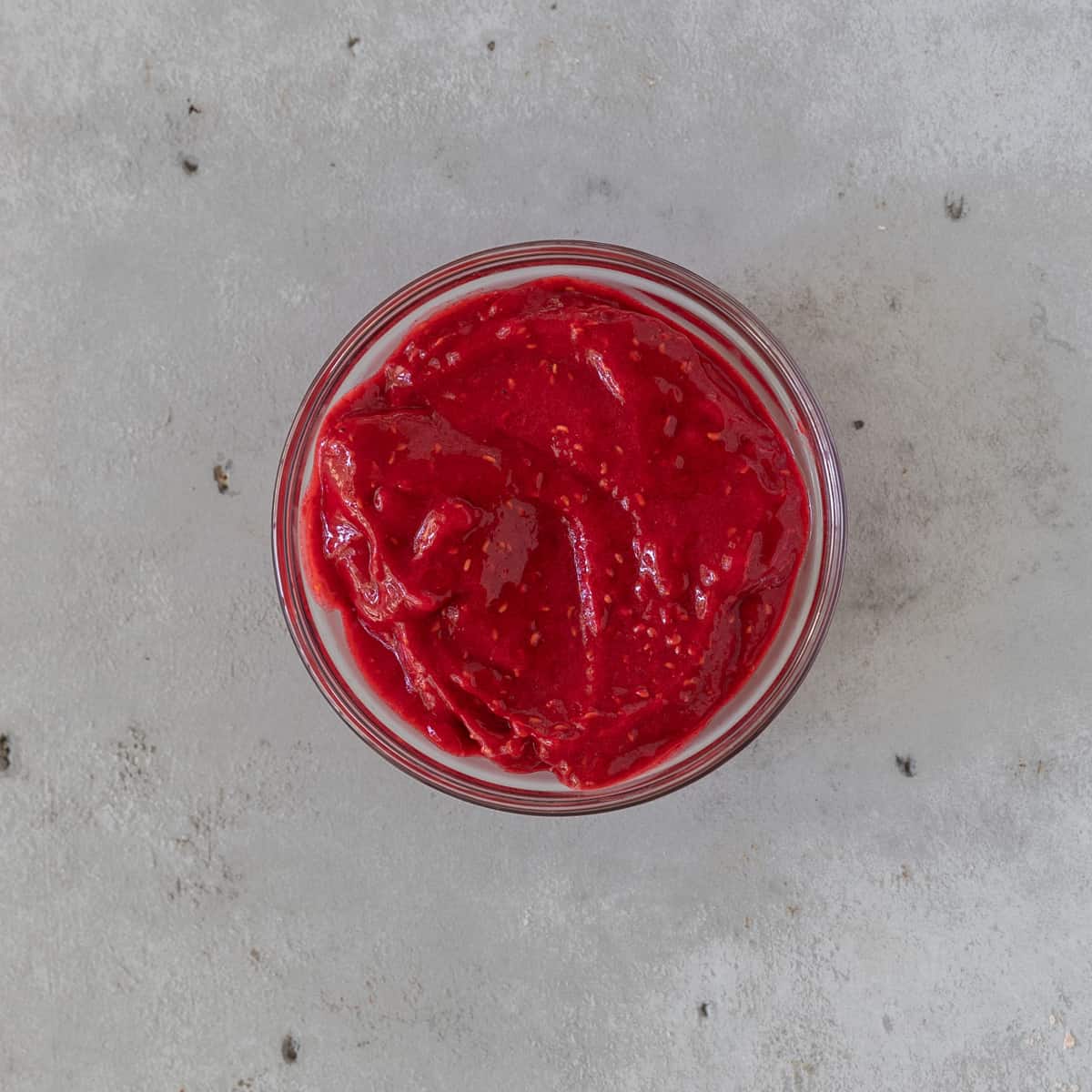 the raspberry sauce in a glass bowl on a grey background.