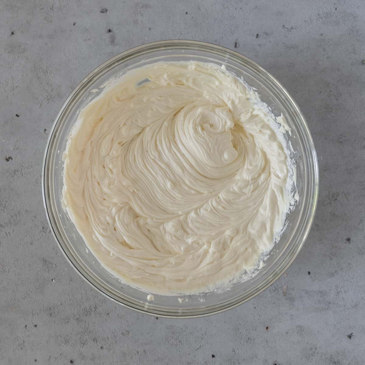 the cream cheese and sugar combined in a glass bowl on a grey background.