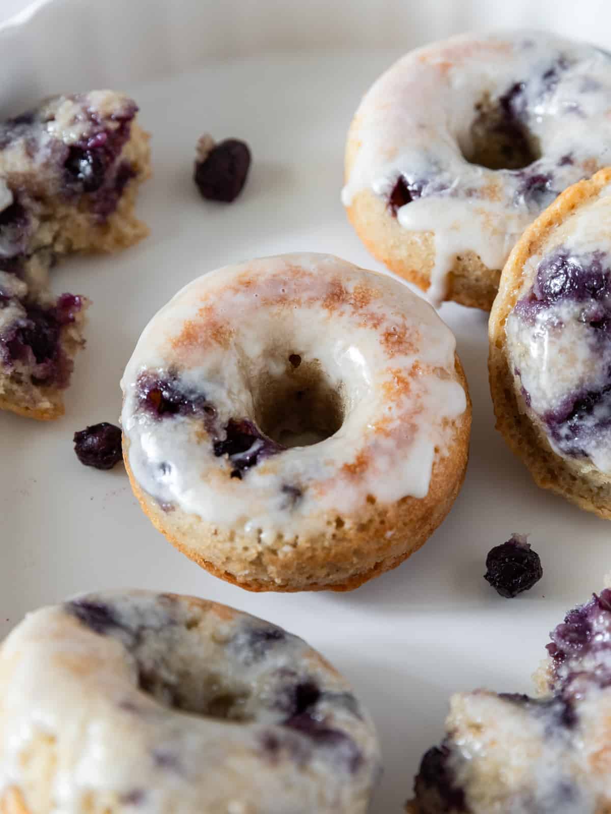 several blueberry donuts on a white background surrounded by fresh blueberries.