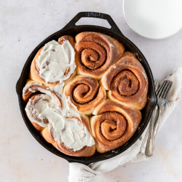 looking down on a cast iron pan filled with caramel cinnamon rolls. half of them are topped with brown butter icing.