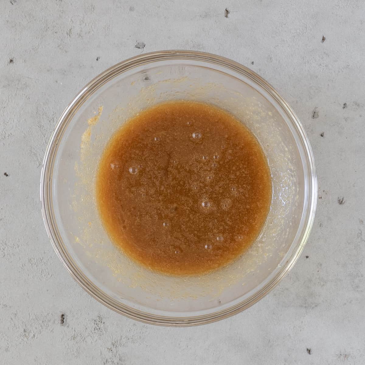 the wet ingredients and brown sugar combined in glass bowl on a grey background.