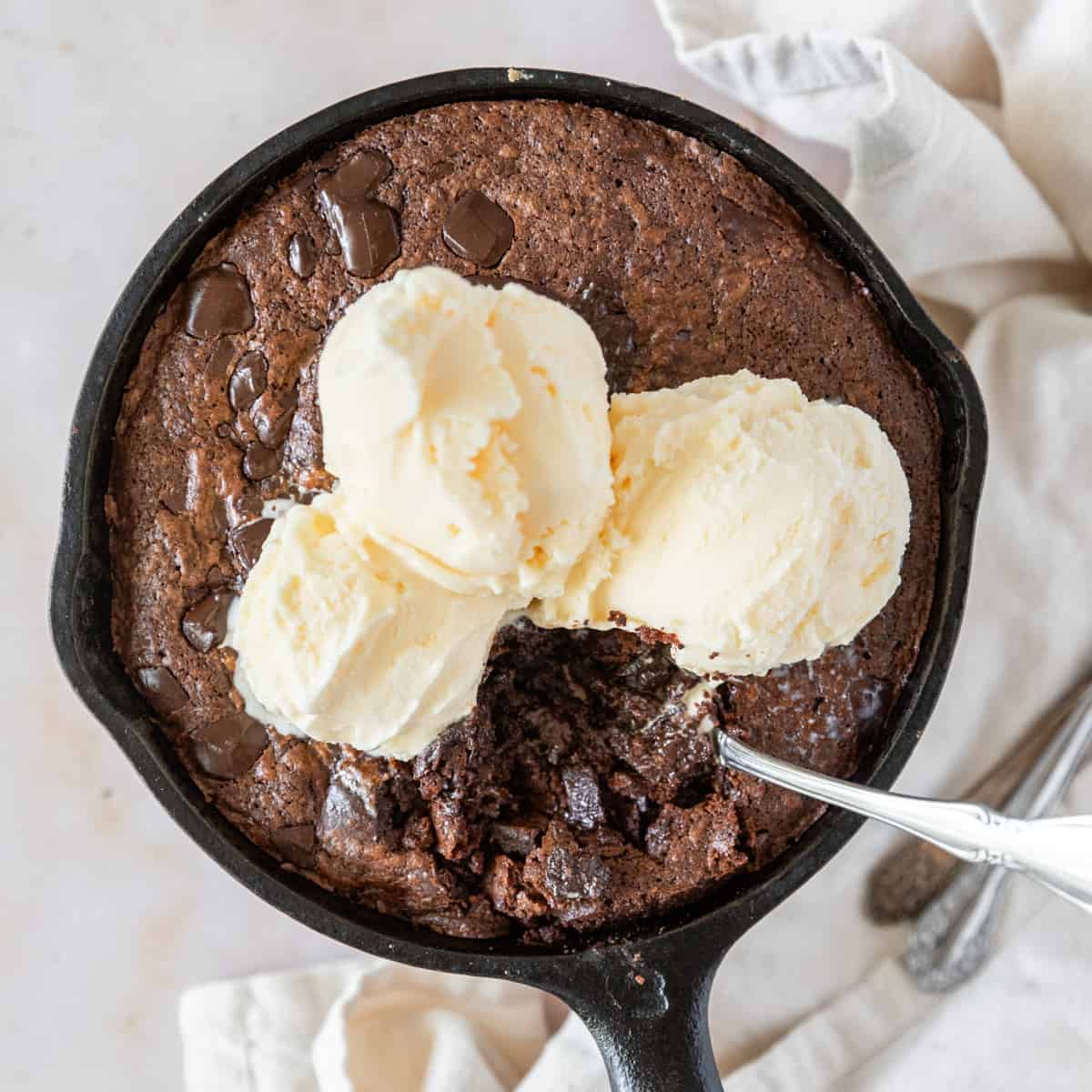 Looking down on a skillet brownie in a cast iron skillet topped with ice cream with a spoon stuck in it.