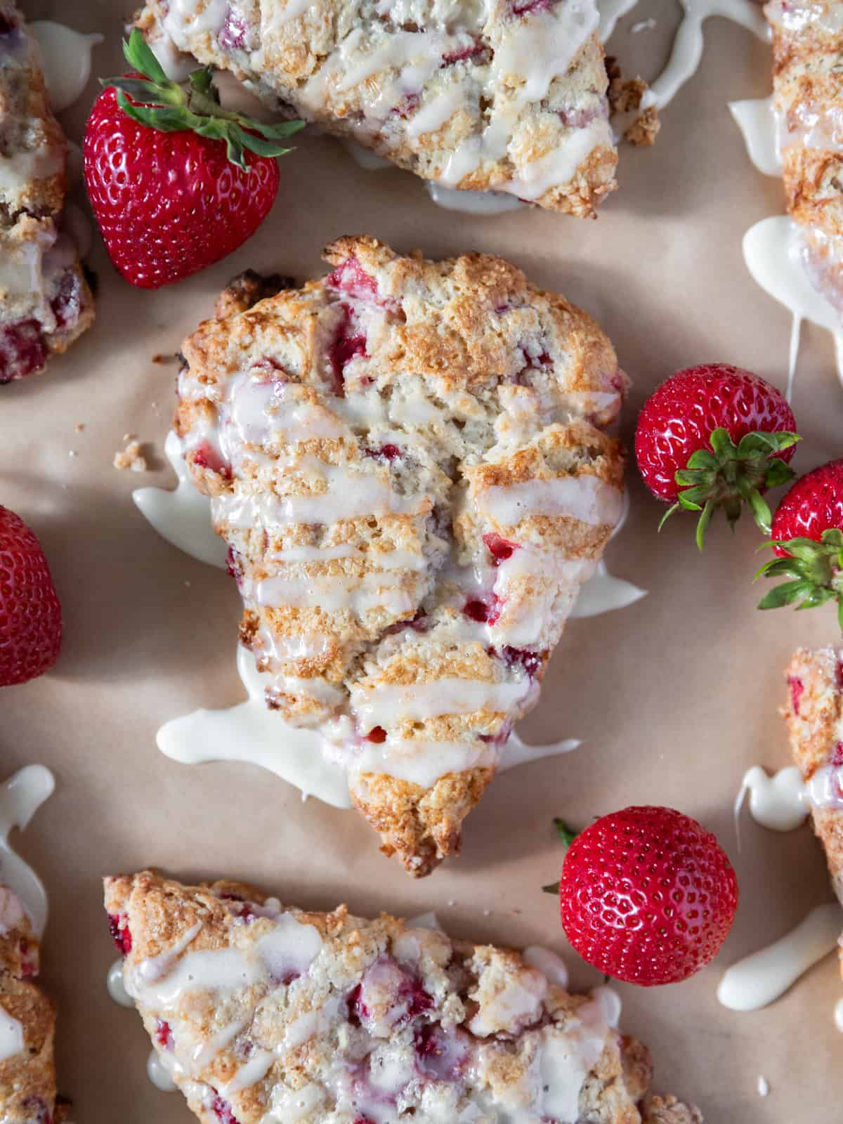 strawberry scones drizzled with vanilla glaze and surrounded by fresh strawberries.