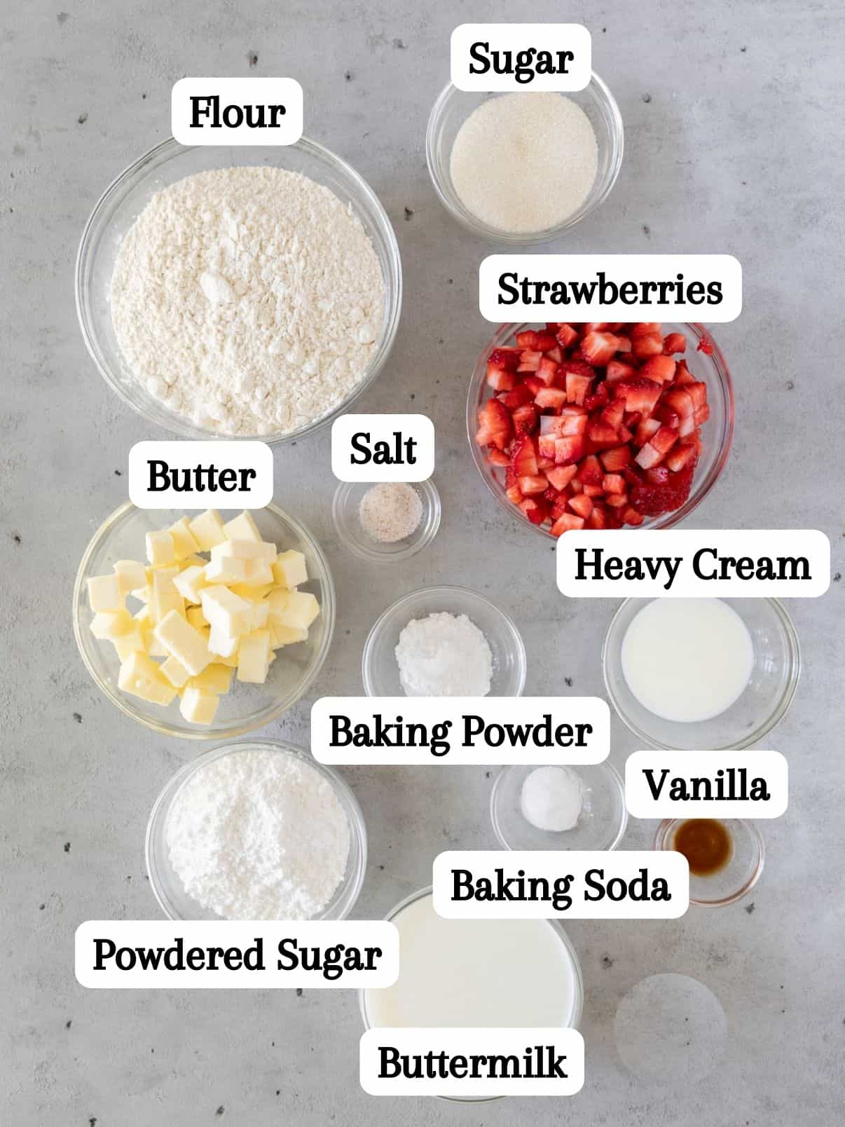 all of the ingredients for this strawberry scones recipe laid out and labeled on a grey background.