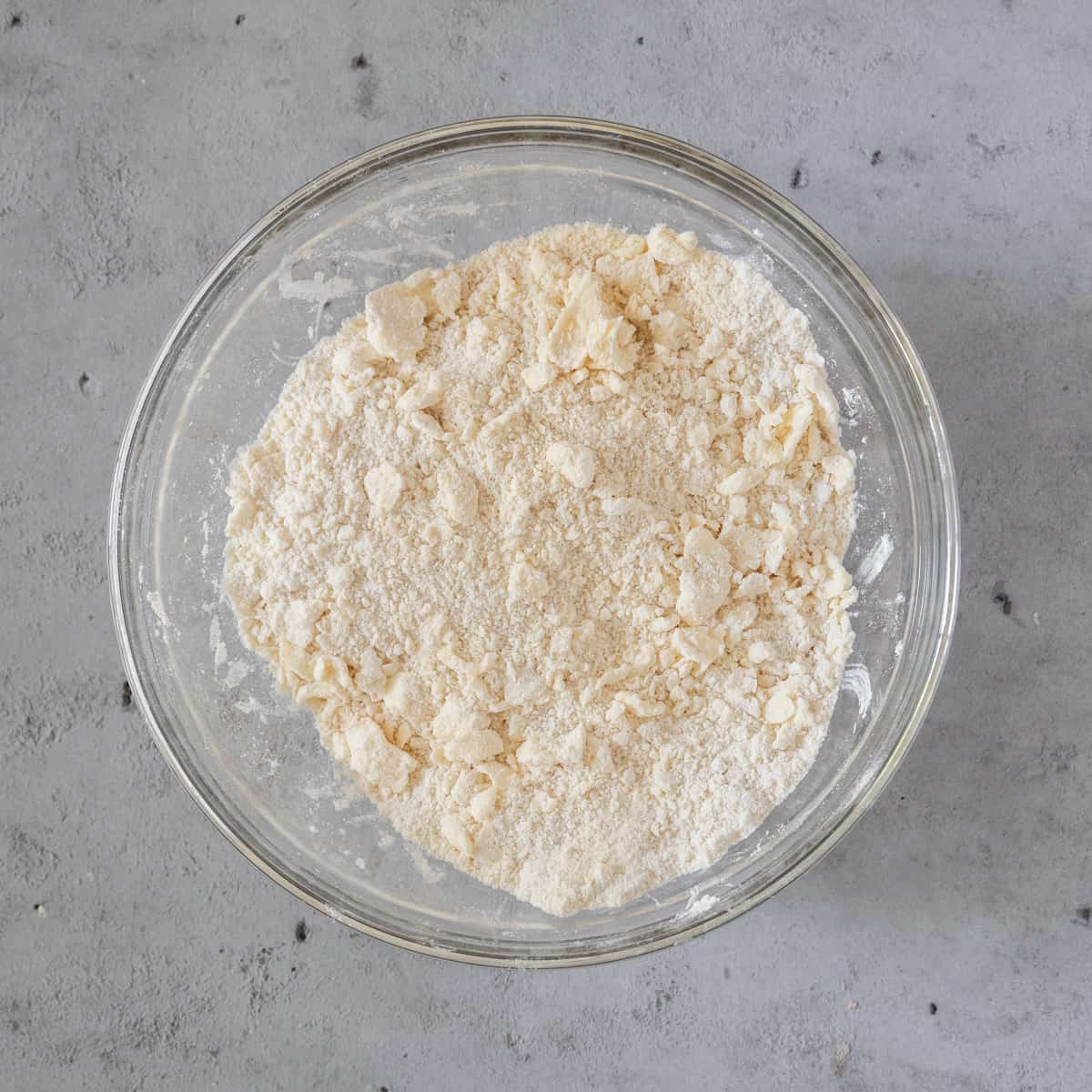 the dry ingredients and butter combined in a glass bowl on a grey background.