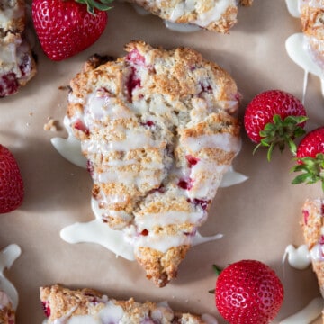 looking down on strawberry scones drizzled with vanilla glaze and surrounded by fresh strawberries.