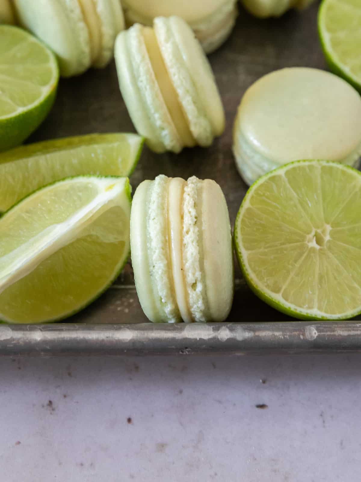 Key Lime Macarons on a sheet pan surrounded by cut up and whole key limes.